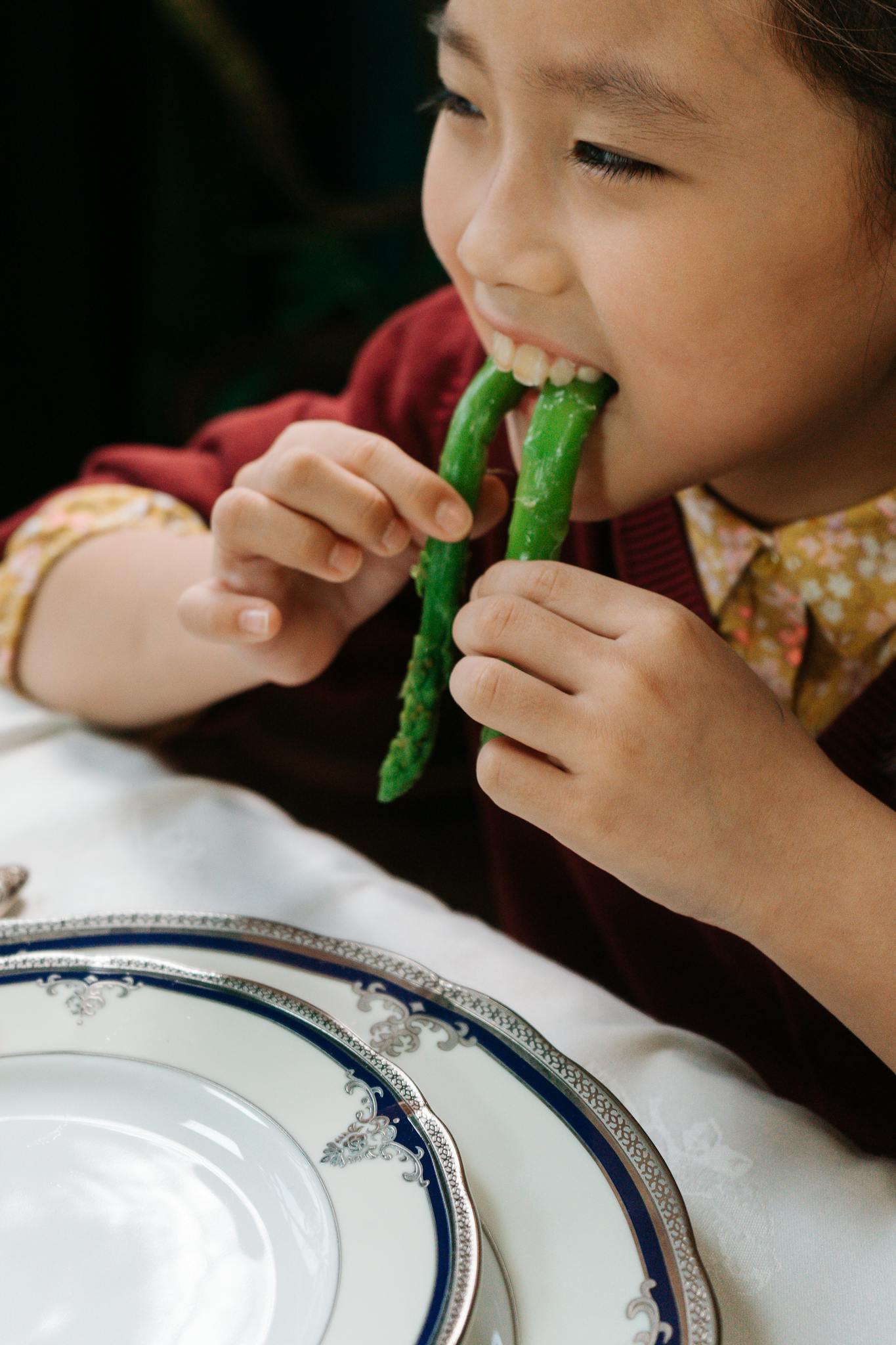 Smiling child enjoying fresh asparagus at a dinner table, promoting healthy eating habits.